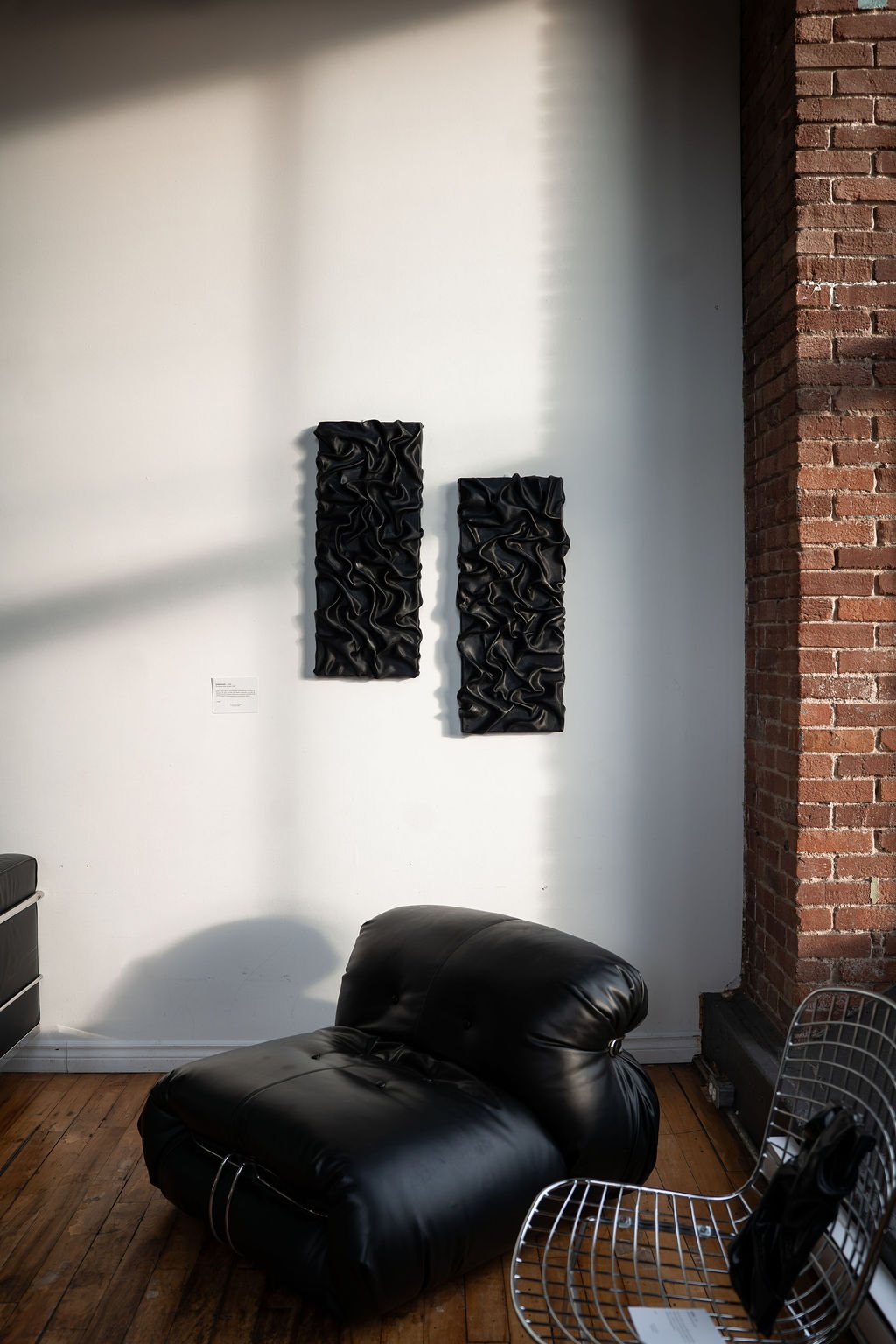 Deux œuvres murales noires texturées au-dessus d’un fauteuil en cuir
