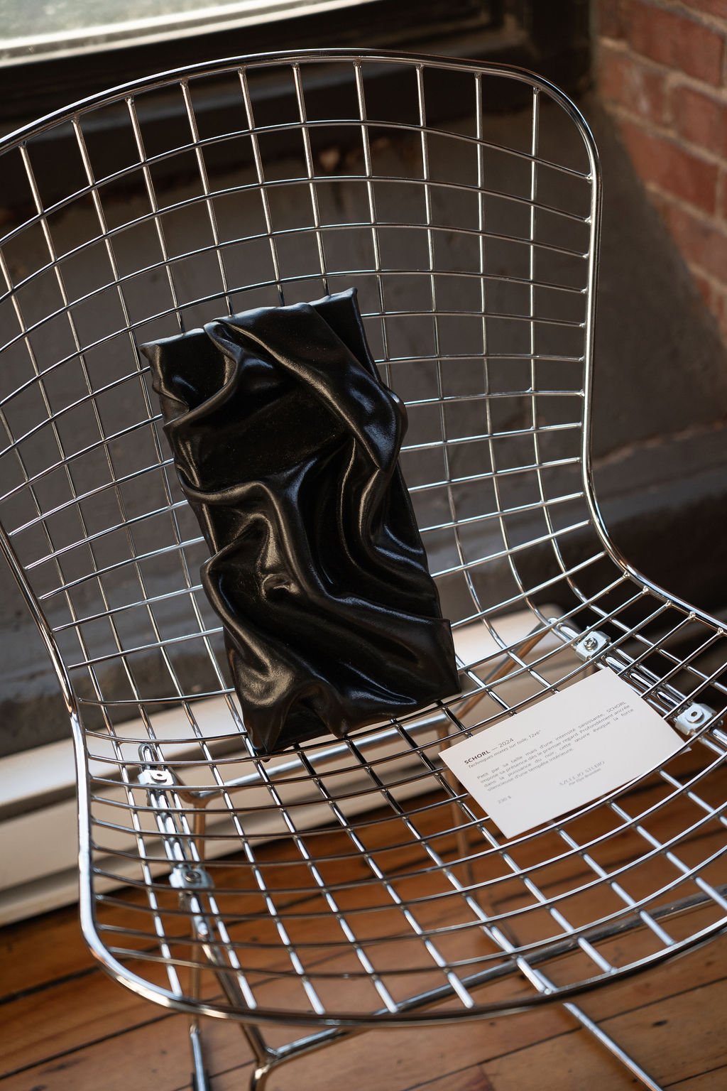 Œuvre sculpturale noire, plissée, posée sur une chaise en fil d’acier