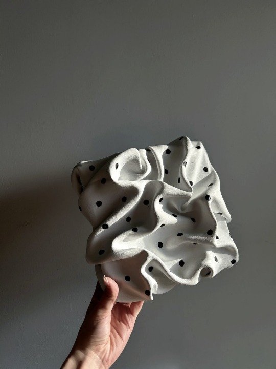 Pièce blanche à pois noirs tenue à la main devant un mur gris