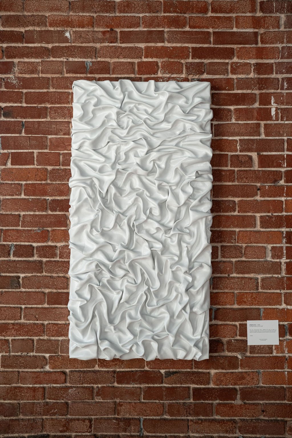 Œuvre blanche texturée sur un mur de briques